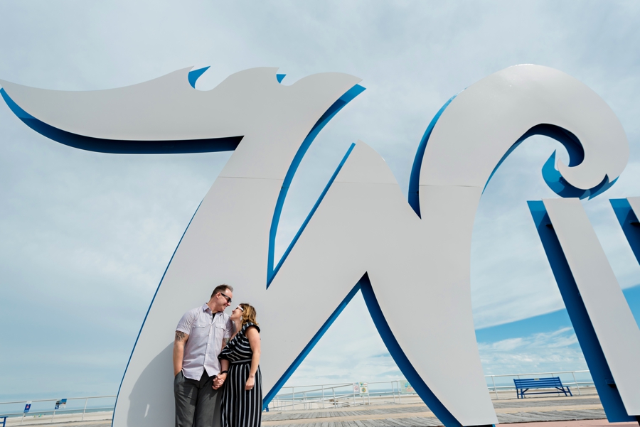 A couple in love lean against the w in the wildwood sign in Long Beach Island for their engagement session.